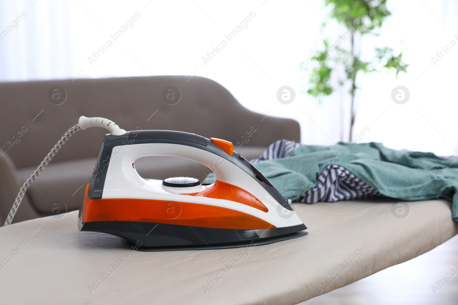 Photo of Modern electric iron and clothes on board indoors. Space for text