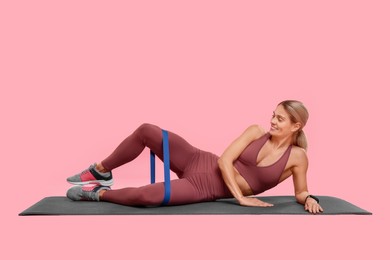 Photo of Woman exercising with elastic resistance band on fitness mat against pink background