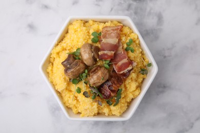 Photo of Cooked cornmeal with bacon, mushrooms and microgreens in bowl on white marble table, top view