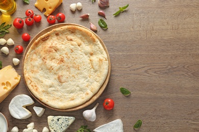 Flat lay composition with pizza crust and fresh ingredients on wooden table, space for text