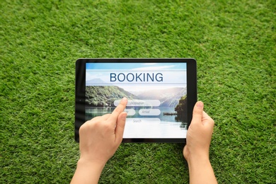 Woman booking tickets online on green grass, closeup. Travel agency concept