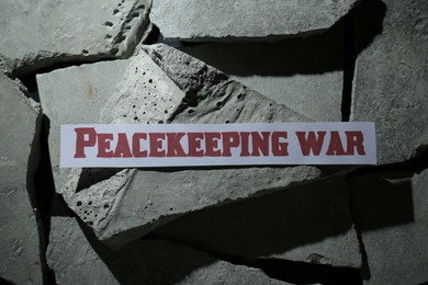 Paper with word Peacekeeping War on pieces of concrete, top view