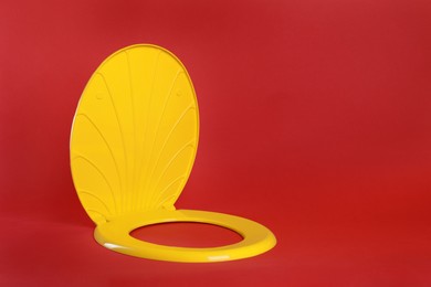 Photo of New yellow plastic toilet seat on red background, space for text