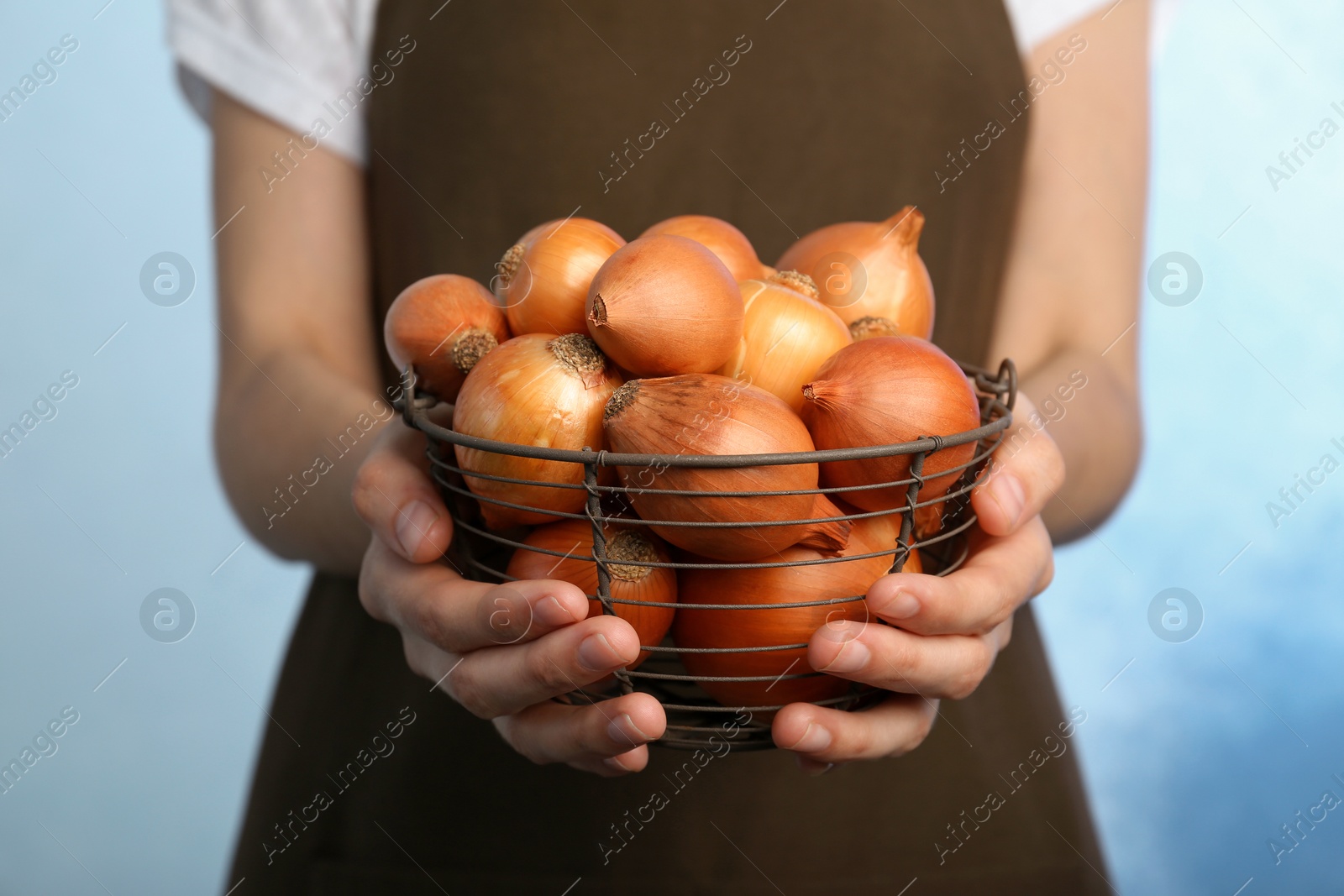 Photo of Woman holding basket with ripe onions on color background