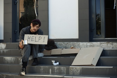 Poor man with mug begging and asking for help on city street