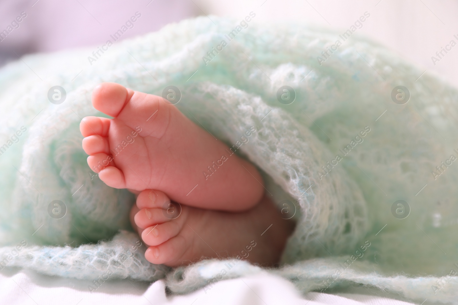 Photo of Cute newborn baby covered in turquoise crocheted plaid on bed, closeup of legs