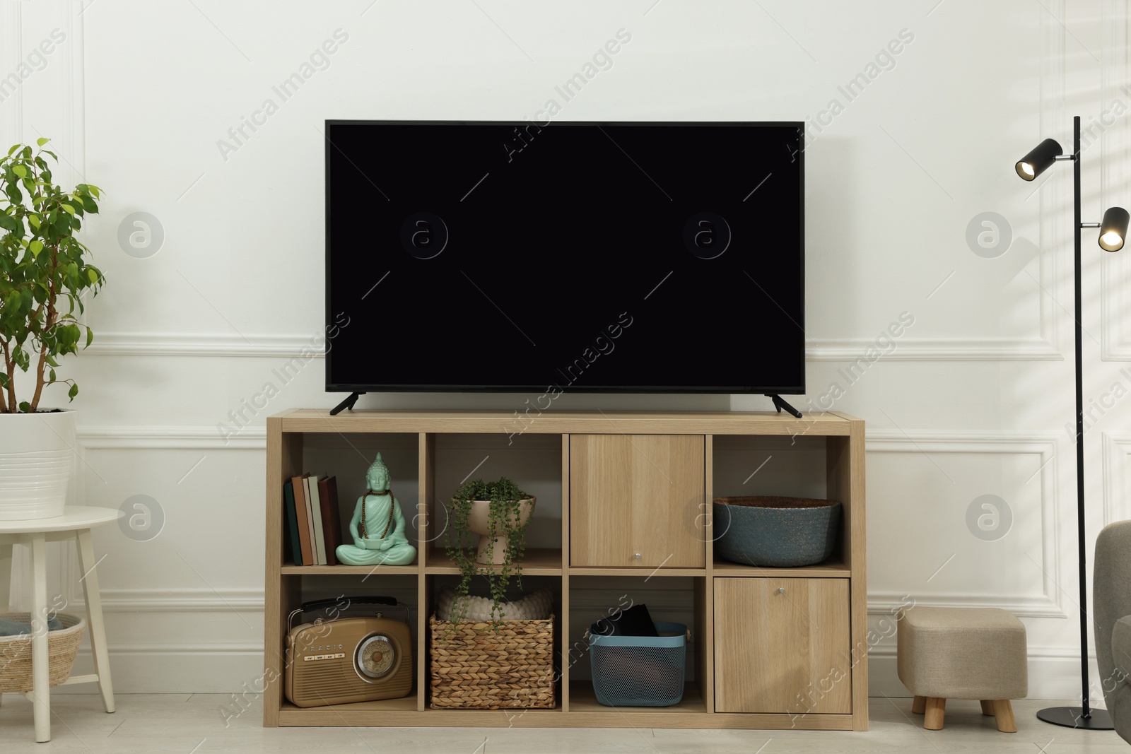 Photo of Modern TV on cabinet, lamp and beautiful houseplant near white wall indoors. Interior design
