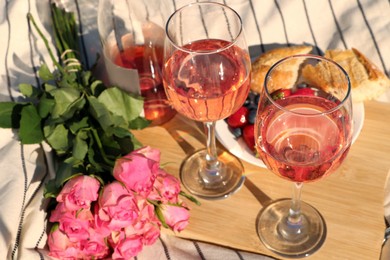 Glasses of delicious rose wine, flowers and food on white picnic blanket