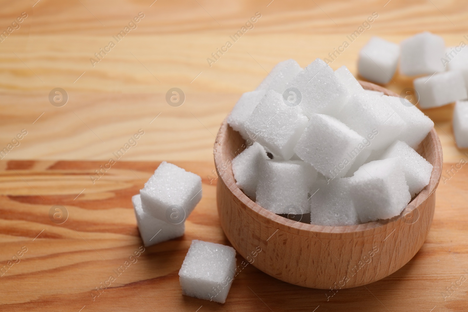 Photo of White sugar cubes in bowl on wooden table, closeup. Space for text