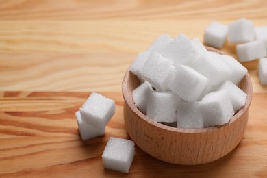 White sugar cubes in bowl on wooden table, closeup. Space for text