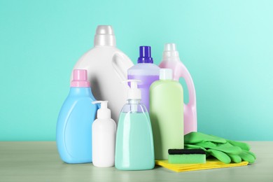 Photo of Different cleaning supplies and tools on wooden table against turquoise background