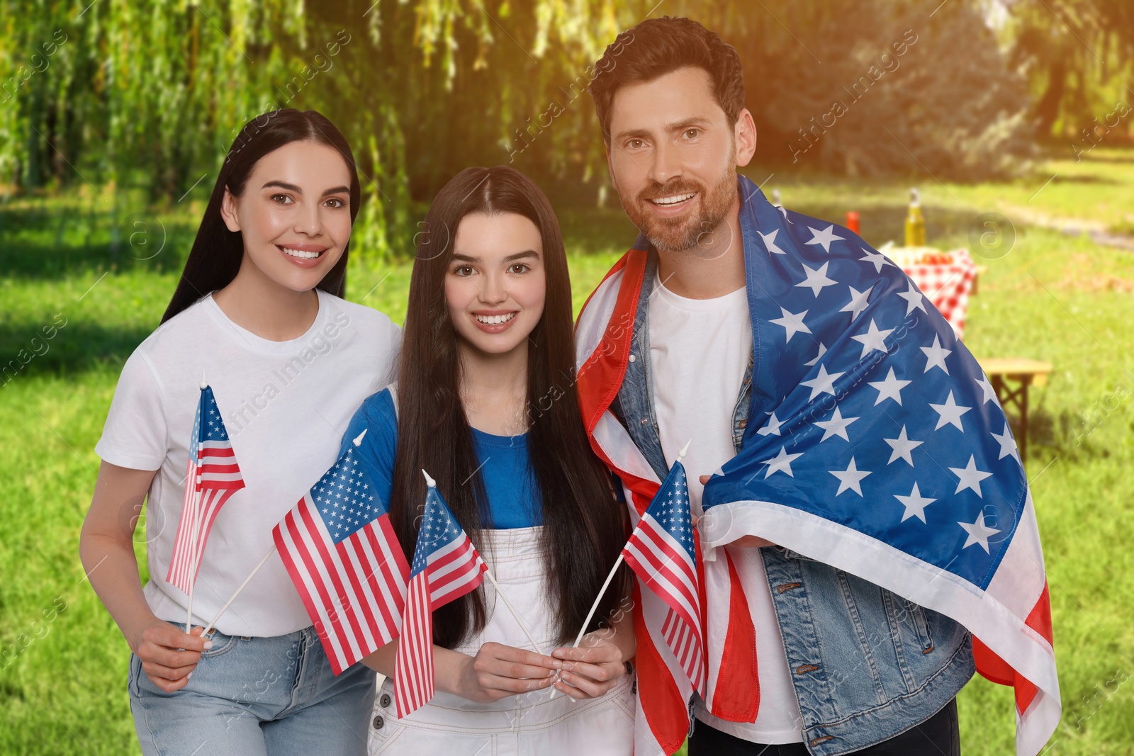 Image of 4th of July - Independence day of America. Happy family with national flags of United States having picnic in park