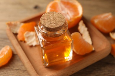Photo of Bottle of tangerine essential oil and peeled fresh fruit on wooden table, closeup