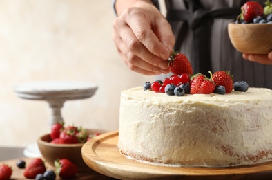 Photo of Woman decorating delicious homemade cake with fresh berries at table indoors, closeup