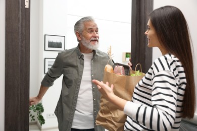 Courier giving paper bag with food products to senior man indoors