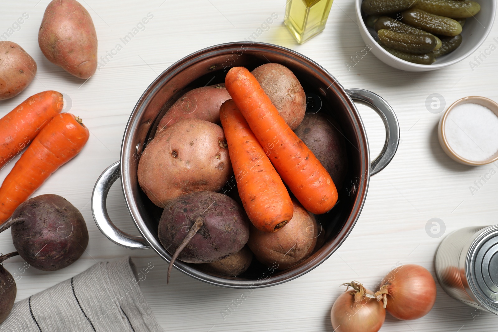 Photo of Fresh vegetables and pot on white wooden table, flat lay. Cooking vinaigrette salad