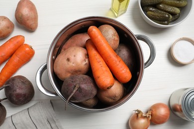 Fresh vegetables and pot on white wooden table, flat lay. Cooking vinaigrette salad