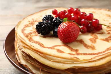Photo of Delicious thin pancakes with berries on plate, closeup
