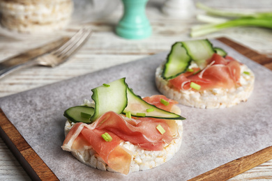 Puffed rice cakes with prosciutto and cucumber on wooden board, closeup