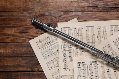 Sheets with musical notes and flute on wooden table, flat lay. Space for text