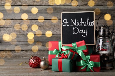Blackboard with phrase St. Nicholas Day, gift boxes and festive decor on wooden table, space for text. Bokeh effect