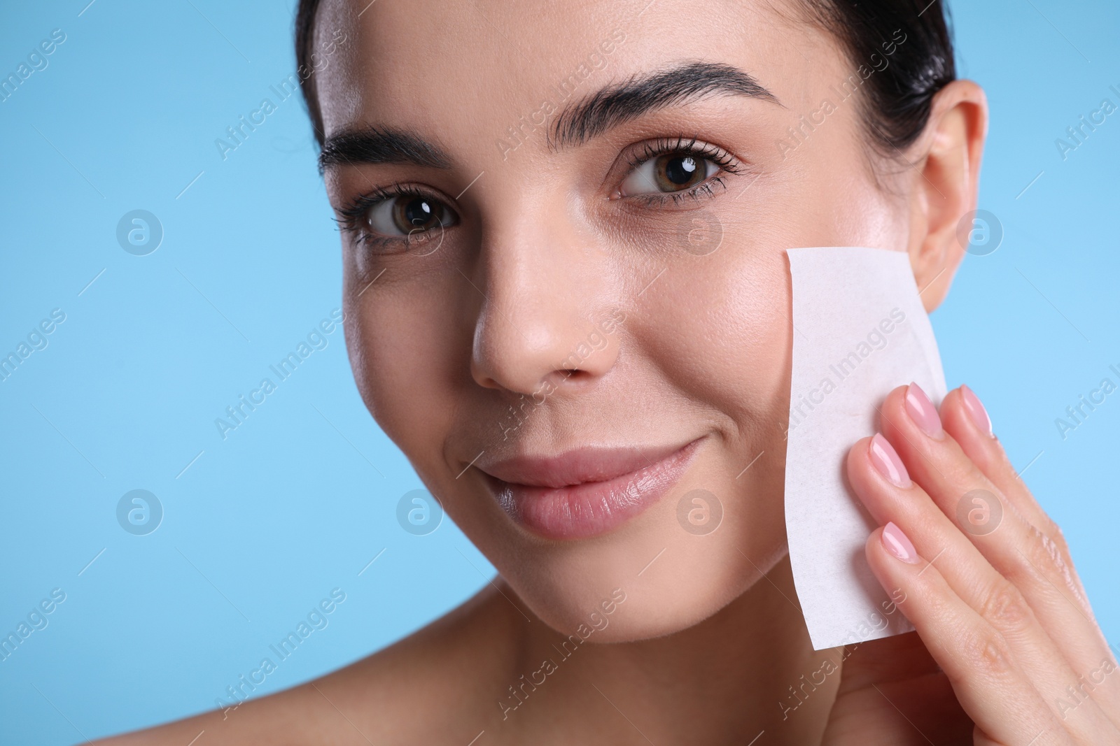 Photo of Beautiful woman using mattifying wipe on light blue background, closeup