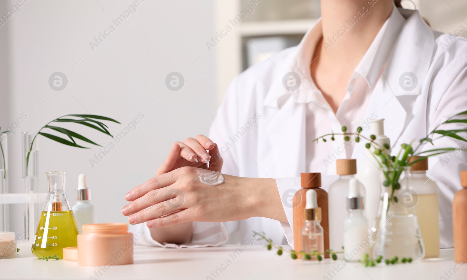 Photo of Dermatologist applying cream onto hand at white table indoors, closeup. Testing cosmetic product