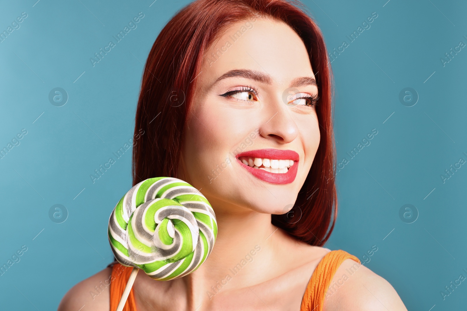 Photo of Happy woman with red dyed hair and green lollipop on light blue background