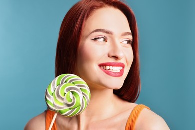 Happy woman with red dyed hair and green lollipop on light blue background