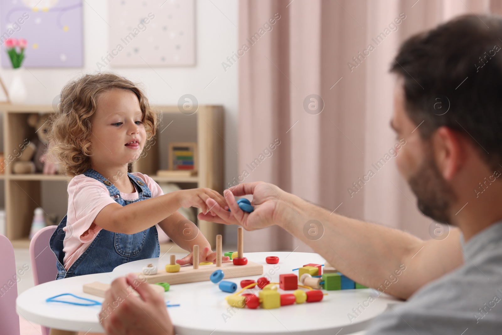 Photo of Motor skills development. Father and daughter playing with stacking and counting game at table indoors