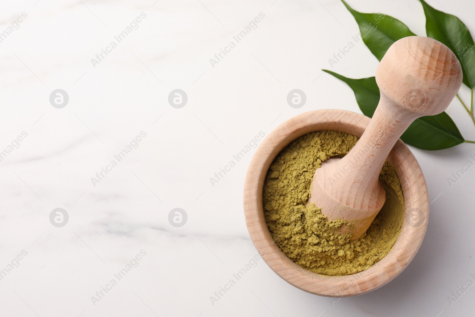 Photo of Mortar of henna powder and green leaves on white marble table, top view with space for text. Natural hair coloring