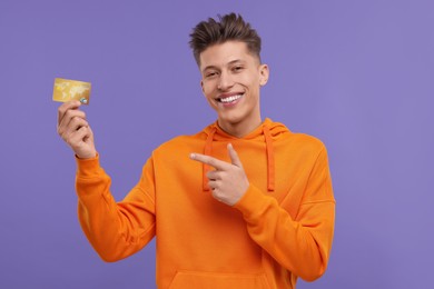 Photo of Happy man pointing at credit card on purple background