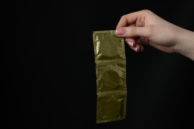 Woman holding condoms on black background, closeup. Space for text