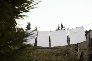 Photo of Bedclothes hanging on washing line near wooden fence outdoors