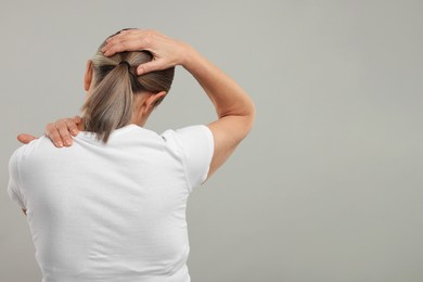 Photo of Mature woman suffering from pain in her neck on grey background, back view. Space for text