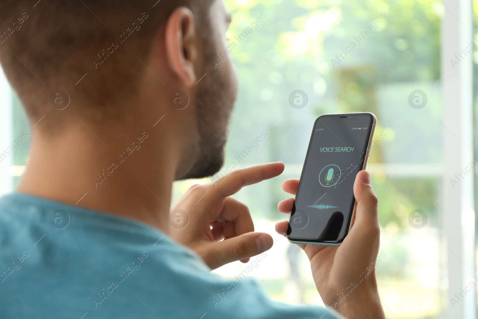 Photo of Young man using voice search on smartphone indoors, closeup