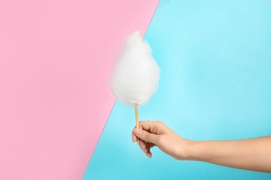 Photo of Woman holding stick with fluffy cotton candy on color background, closeup