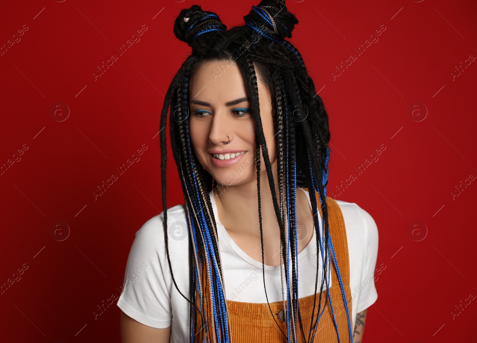 Photo of Beautiful young woman with nose piercing and dreadlocks on red background