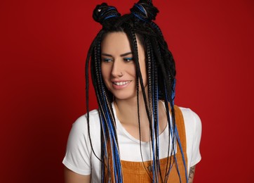 Photo of Beautiful young woman with nose piercing and dreadlocks on red background