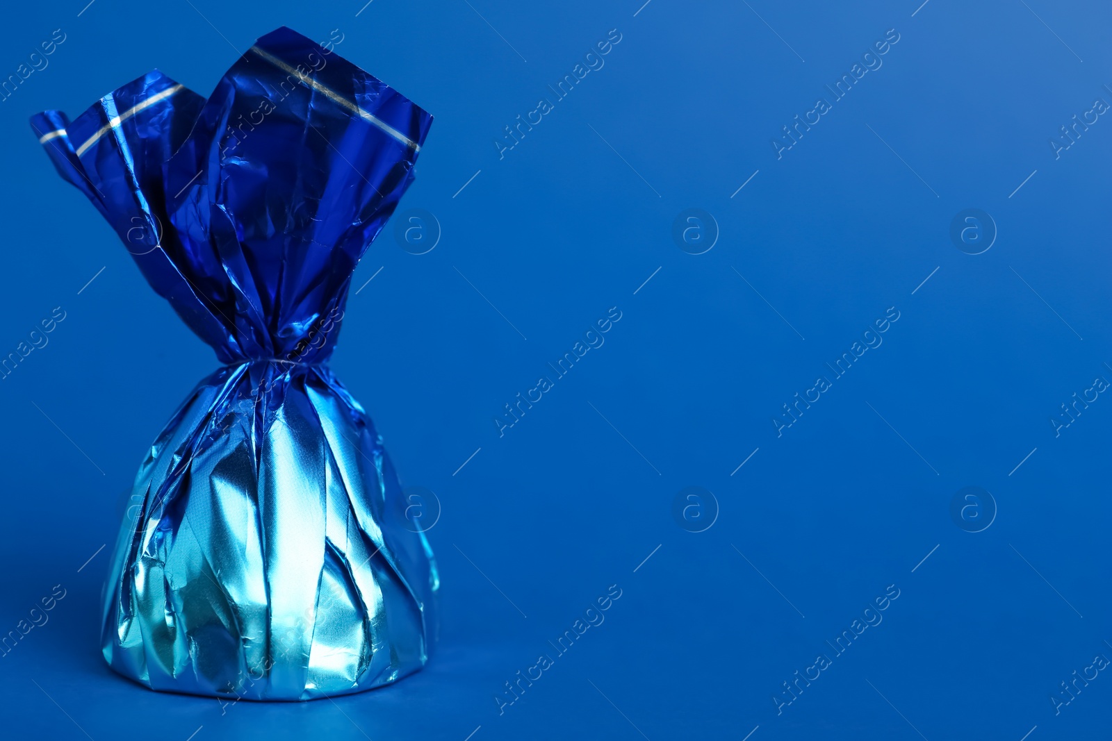 Photo of Candy in bright wrapper on blue background. Space for text