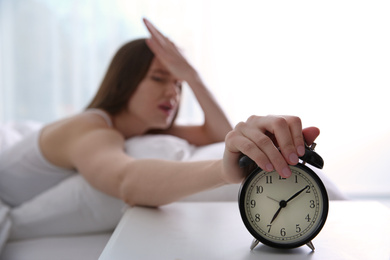 Young woman turning off alarm clock at home in morning, focus on hand