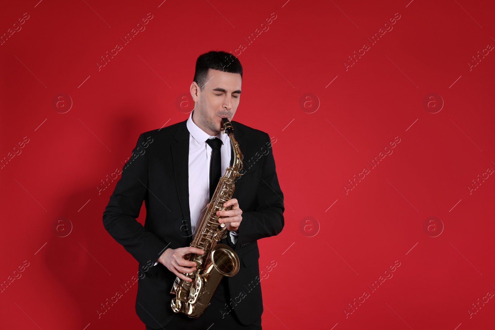 Photo of Young man in elegant suit playing saxophone on red background