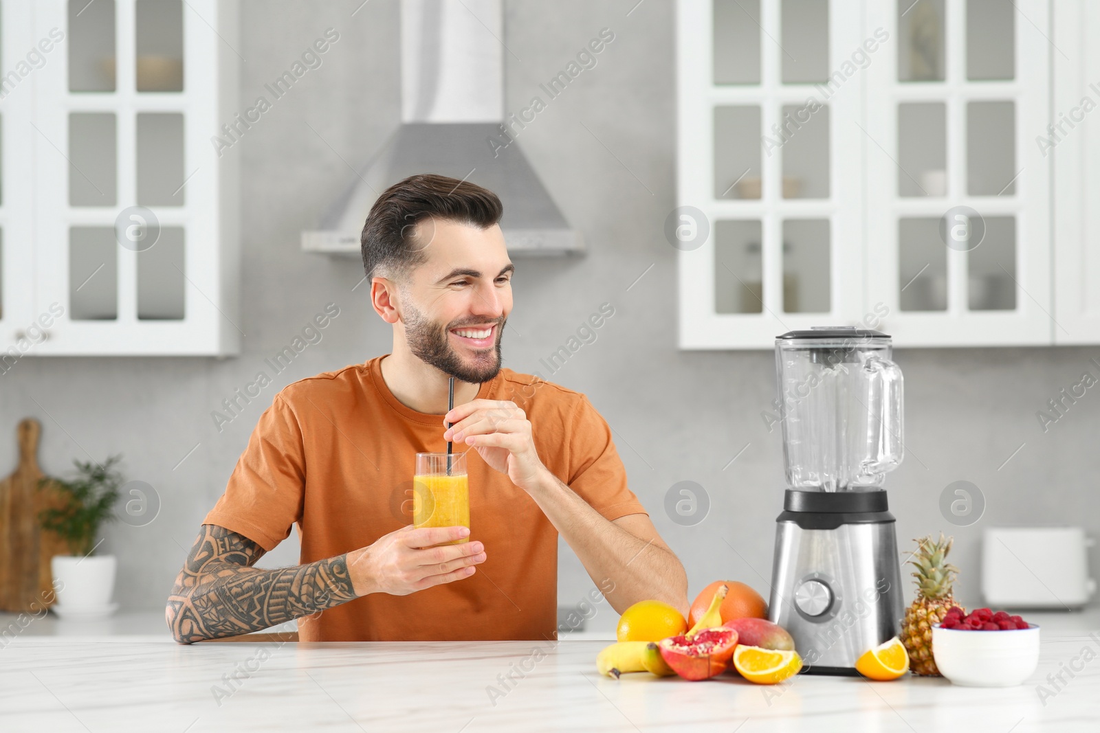 Photo of Handsome man with delicious smoothie at white marble table in kitchen