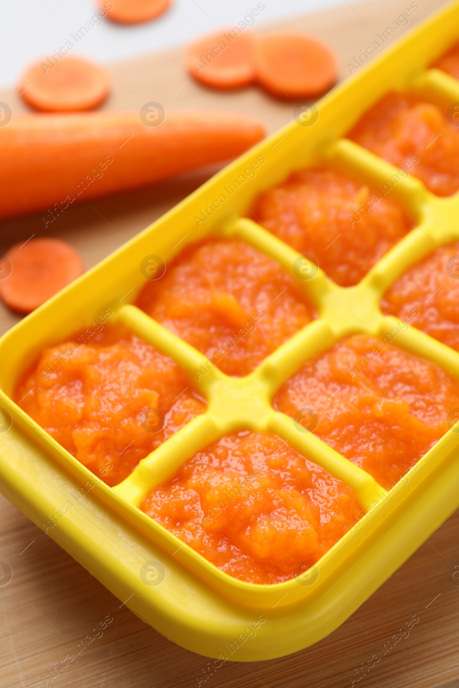 Photo of Carrot puree in ice cube tray on wooden board, closeup. Ready for freezing