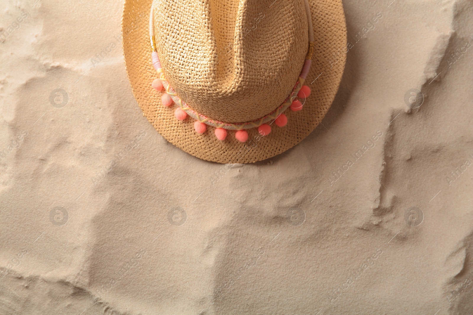 Photo of Stylish straw hat on sand, top view. Space for text