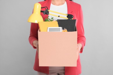 Unemployed woman with box of personal office belongings on grey background, closeup