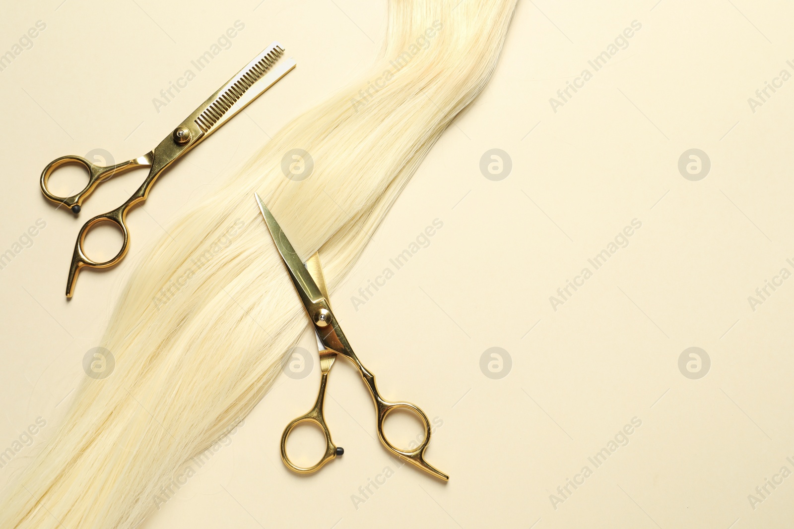 Photo of Professional scissors with blonde hair strand on beige background, flat lay. Space for text