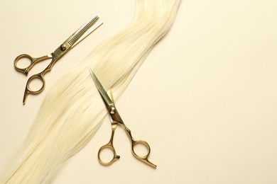 Professional scissors with blonde hair strand on beige background, flat lay. Space for text