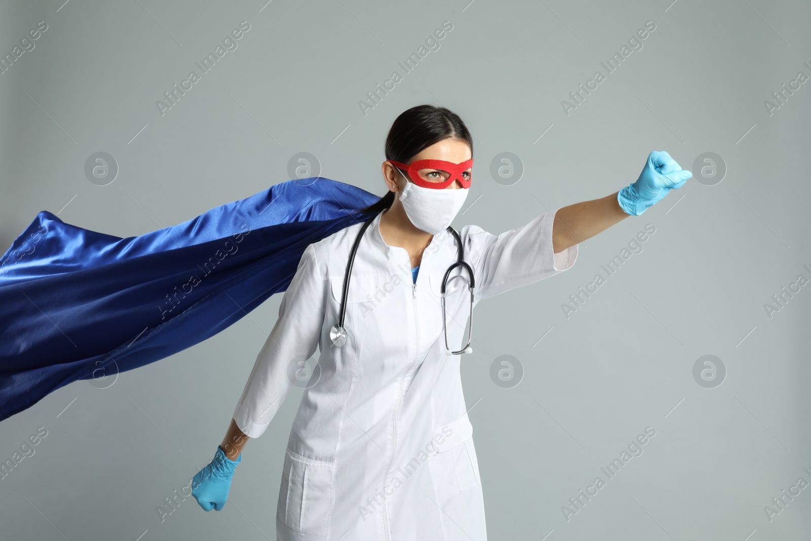 Photo of Doctor dressed as superhero posing on light grey background. Concept of medical workers fighting with COVID-19