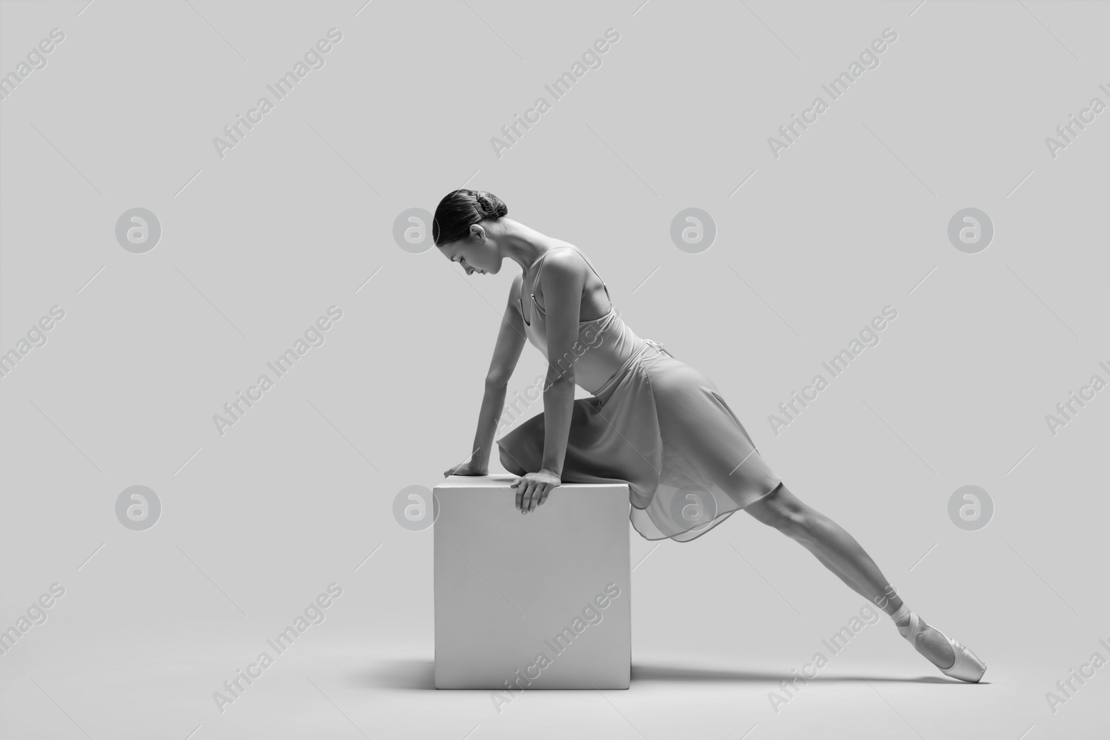 Photo of Young ballerina practicing dance moves on cube, toned in black and white